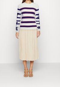 Striped knit sweater in white, navy, and red; pleated beige midi skirt; strappy beige sandals; floral details on sleeves.