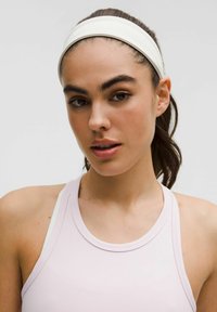 Light pink athletic tank with a rounded neckline, worn beneath a white headband. Smooth, stretchy fabric, designed for comfort during activities.