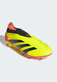 Crampons de football jaunes avec des rayures noires, un haut en maille noir ajusté comme une chaussette, et des accents roses. Le haut texturé et les pointes translucides améliorent l'adhérence.