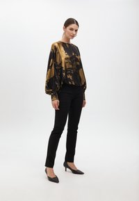 Blusa tie-dye nera e oro con maniche a palloncino, abbinata a pantaloni neri aderenti e décolleté neri a punta. Tessuto liscio e lucido.