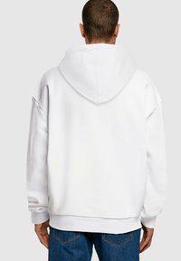 Hanorac alb supradimensionat cu o glugă mare, umeri lăsați și manșete ribbate. Fabricat dintr-un material moale, cu un design minimalist fără logo-uri vizibile.