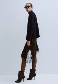 Czarny prążkowany sweter, przezroczysta czarna spódnica z koronkową lamówką, czarne rajstopy i botki na szpilce. Modelka nosi ciemne okulary przeciwsłoneczne.