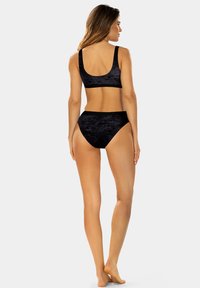 Czarny zestaw bikini z miękkiej, teksturowanej tkaniny. Biustonosz ma dekolt z tyłu i szerokie ramiączka, a dolna część charakteryzuje się wysokim stanem i minimalnym zakryciem.