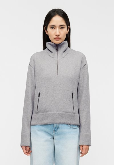 Sweat-shirt en polaire grise avec col montant, fermeture éclair au quart sur le devant et deux poches latérales zippées. Présente une coupe décontractée et des poignets côtelés.