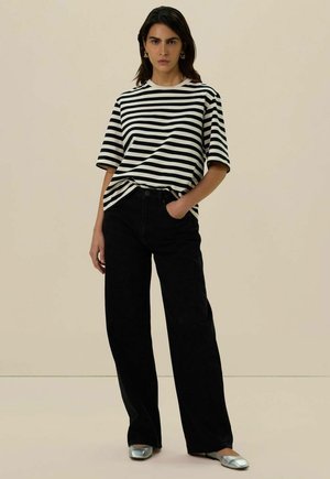 T-shirt rayé noir et blanc avec une coupe décontractée, associé à un jean noir taille haute et des chaussures plates argentées. Tissu lisse et léger.