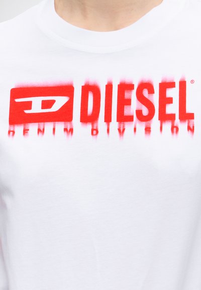 Крупен план на бяла риза с червен логотип на Diesel и текст, който изглежда леко размазан или избледнял отдолу.