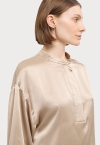 Beige satengbluse med høy krage, knappelukking og løse ermer. Glatt tekstur og lett utseende.