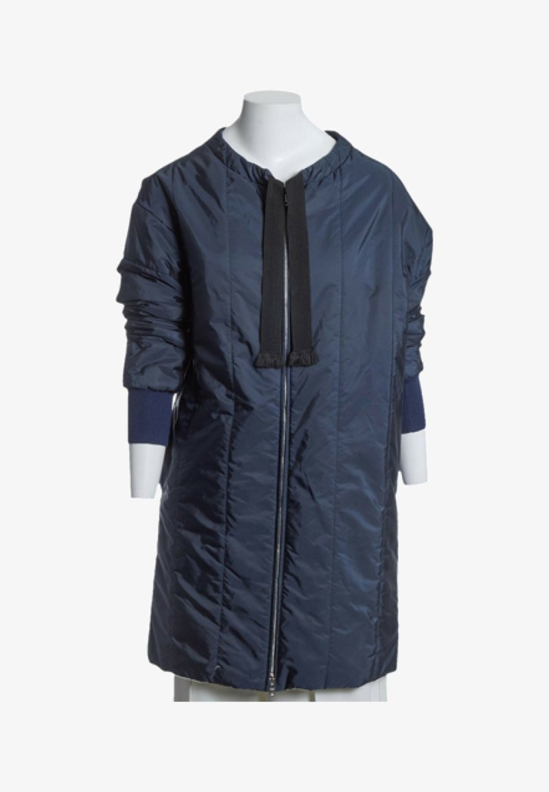Manteau long matelassé bleu marine avec fermeture éclair intégrale à l'avant, détails de bordure noire et manches froncées s'étendant jusqu'aux poignets ajustés.