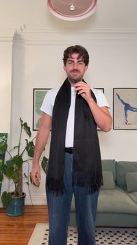 Črna ruta iz mehkega materiala, z resicami na koncih. Nošena preko belega srajca, spodaj pa so vidne modre kavbojke. Notranji okolje.