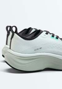 Paire de chaussures de sport blanches et noires avec semelles épaisses et texturées ainsi que des languettes à l'arrière, vues de dos et de profil.