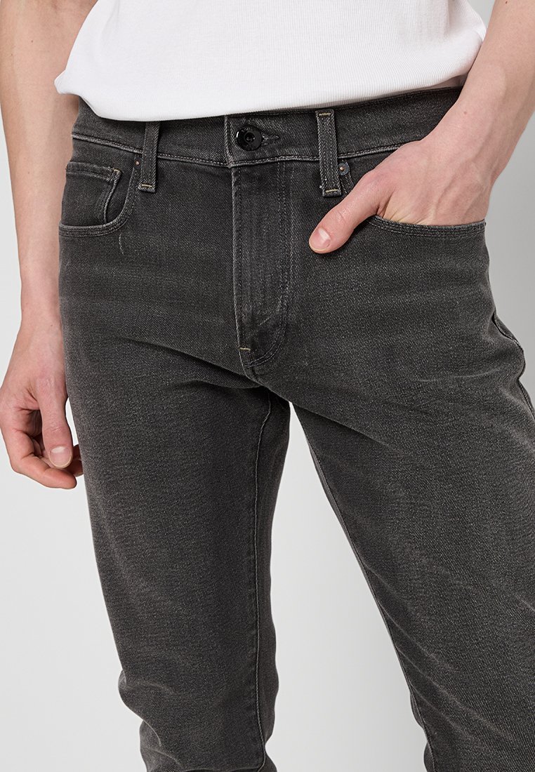 Donkergrijze denim jeans met een slim fit, voorzien van een voorzak, subtiele vervaging en een knoopsluiting. De stof heeft een gladde textuur.