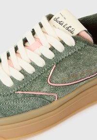 Baskets en daim vert avec des accents roses, surface texturée, lacets crème et semelle en caoutchouc beige ; présente une étiquette sur la languette.