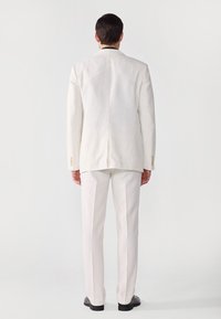 Helle Anzüge mit maßgeschneiderter Passform. Verfügt über einen einzelnen Schlitz, minimale Details und gerade geschnittene Hosen. Gepflegte Stoffe und elegantes Design.