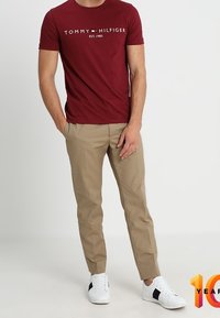 Rød bomulds T-shirt med hvid logo tekst, parret med beige bukser og hvide sneakers med sorte accenter.