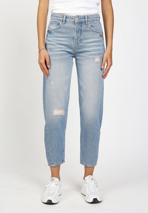 Light blue high-waist distressed jeans worn with white sneakers and a white top, showing front view from waist to ankles.