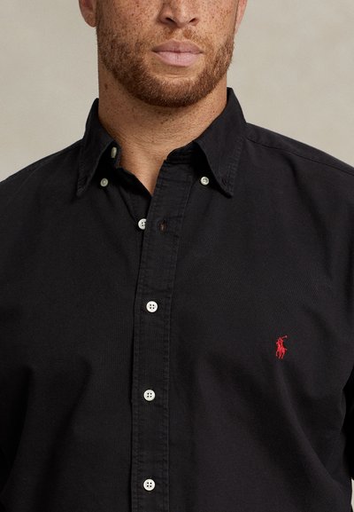 Svart bomullskjorte med knapper, med spiss krage, hvite knapper og en liten rød polo-logo på brystet.