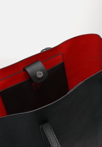 Sac en cuir noir avec une texture lisse et un haut ouvert, présentant un intérieur rouge vif et un rabat en cuir noir avec un fermoir à pression en argent.