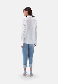 Weißes Langarmhemd mit Lochmuster, kombiniert mit hellblauen hochgekrempelten Jeans und blauen High Heels.