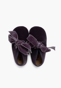 Zapatillas de terciopelo en púrpura oscuro con amplios lazos de terciopelo en la parte delantera, punteras redondeadas y forro interior suave, con un diseño sencillo.