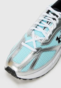 Svijetloplavi atletski tenisice s mrežastim gornjištem, srebrnim detaljima, bijelim vezicama i teksturiranom gumenom potplatom. Prisutni su istaknuti logotip Under Armour.