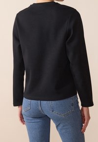Sweat-shirt noir à manches longues avec un col rond et une texture lisse, associé à un jean denim bleu clair avec une conception classique à cinq poches.
