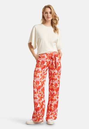 White short-sleeve top with relaxed fit, paired with orange floral print pants featuring a tie waist and wide legs, worn with white sneakers.
