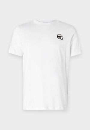 Hvid bomulds-t-shirt med et lille sort og hvidt grafik på venstre brystområde. Klassisk rund hals og korte ærmer.