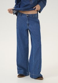 Wide-leg denim jeans in medium blue wash, featuring a button closure, five-pocket design, and a straight hem with contrasting stitching.