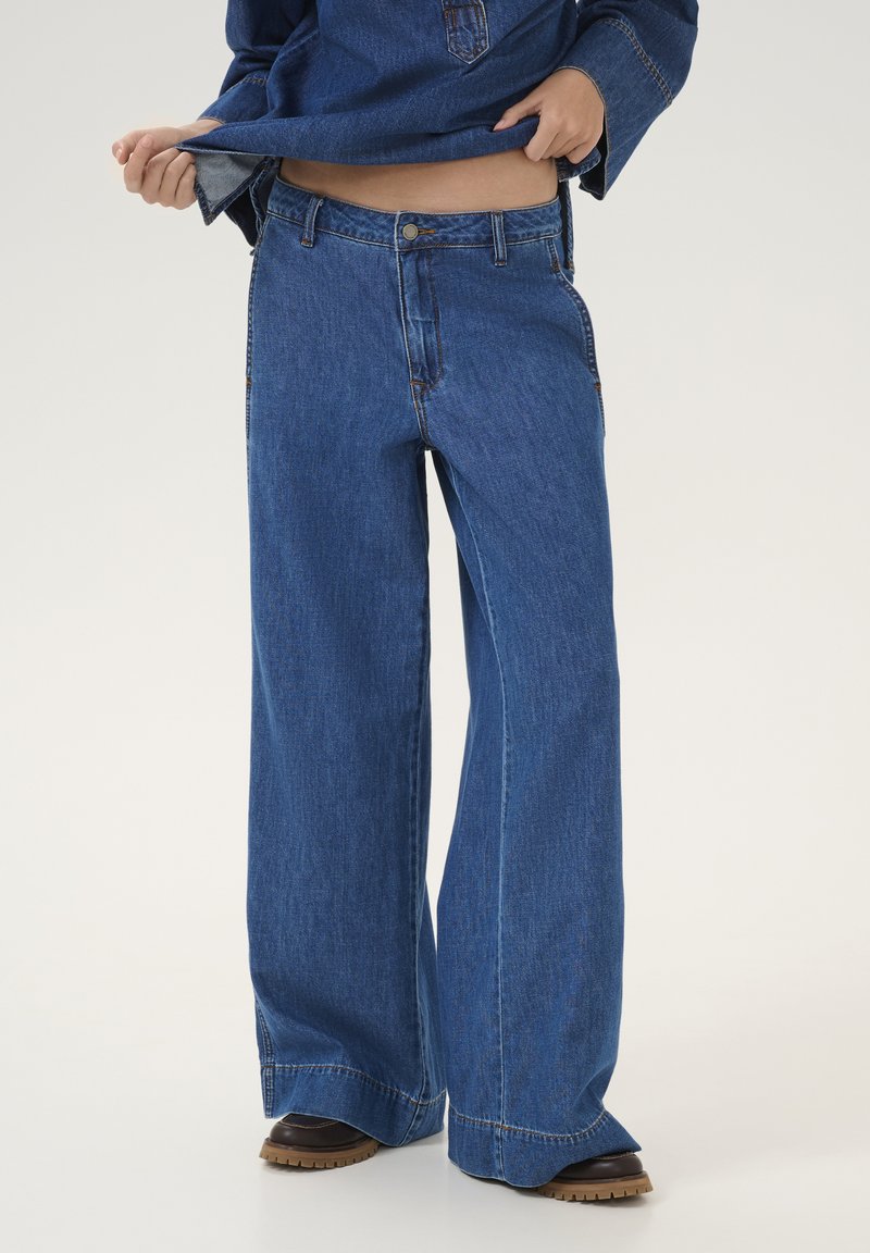 Wide-leg denim jeans in medium blue wash, featuring a button closure, five-pocket design, and a straight hem with contrasting stitching.