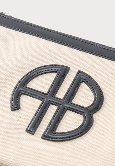 Čierne prešívané kožené logo v tvare štylizovaných písmen "A" a "B" na béžovej textúrovanej látke s čiernym lemom hore.