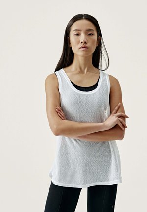 White sleeveless top with a textured pattern, round neckline, and relaxed fit, layered over a black tank top. Paired with black leggings.