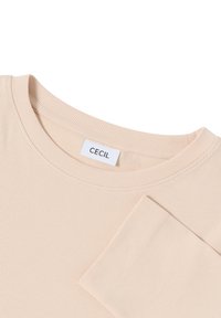 Beige ribattu pitkähihaine paita, jossa on pyöreä pääntie ja hihansuissa resorit. Merkki "CECI" on näkyvissä pääntien sisäpuolella. Sileä pinta.