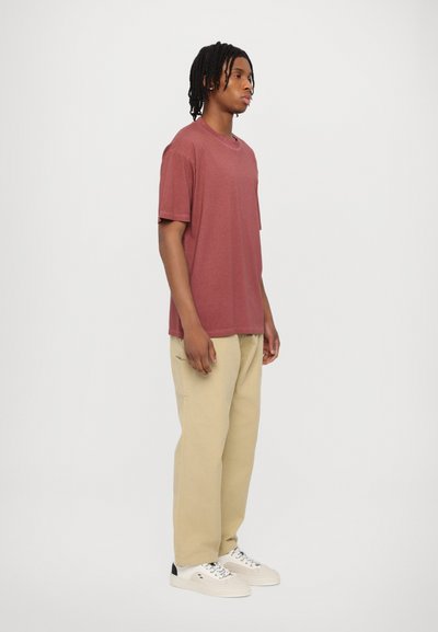 Camiseta de manga corta burdeos, corte relajado, combinada con pantalones beige y zapatillas blancas. Diseño sencillo sin patrones ni adornos.