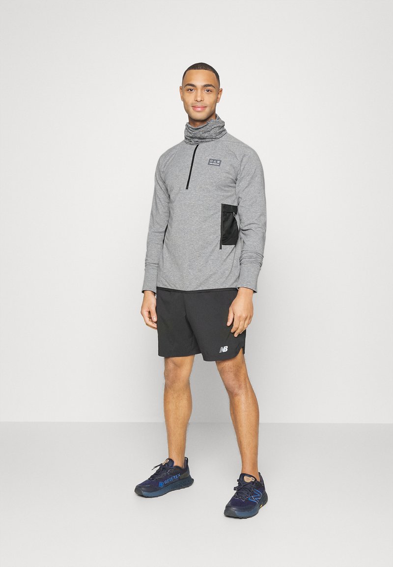 Suéter gris de manga larga con media cremallera y detalle de bolsillo negro, combinado con pantalones cortos negros y zapatillas deportivas azules. Textura suave.