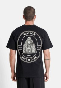 Zwarte katoenen t-shirt met een grote wittearchitectonische afbeelding op de achterkant, met de tekst "MAISON" en "SIXTH JUNE", korte mouwen.