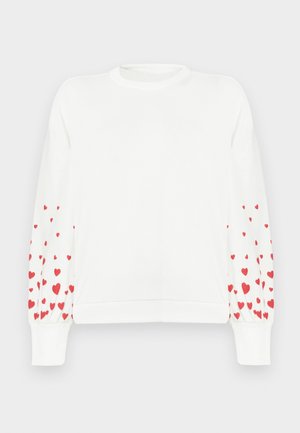 Hvit genser med lange ermer som har et mønster av små røde hjerter langs de ytre armene. Ribbet halslinning og mansjetter.