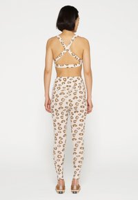 Bralette e leggings con stampa leopardata in beige con macchie marroni. Presenta spalline incrociate regolabili e una vestibilità aderente. Cuciture piatte.
