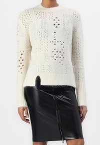 Krämfärgad stickad tröja med ett texturerat mönster som har olika hål och detaljer i mörkare nyanser. Kombinerad med en slank svart läderkjol.