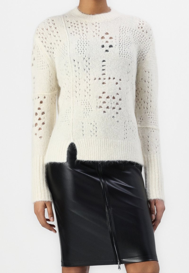 Krämfärgad stickad tröja med ett texturerat mönster som har olika hål och detaljer i mörkare nyanser. Kombinerad med en slank svart läderkjol.
