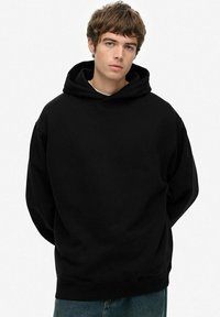 Sudadera negra con capucha que cuenta con cordones y bolsillo canguro, hecha de una tela suave con un corte relajado y puños de canalé. Diseño simple sin patrones.
