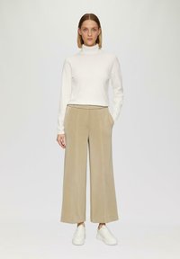 Beige weite Hosen mit Seiten Taschen und einer glatten Textur, kombiniert mit einem maßgeschneiderten weißen Rollkragenpullover, ergänzt durch weiße Sneakers.