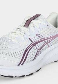 Λευκό αθλητικό παπούτσι με μοβ λογότυπο Asics, λευκά κορδόνια και επάνω μέρος από αναπνέον πλέγμα, εμφανιζόμενο από πλάγια εμπρός γωνία.