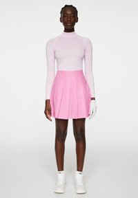 Pitkähiha, vaaleanpunainen paita, jossa on valkoisia yksityiskohtia, yhdistetty vaaleanpunaiseen laskostettuun hameeseen, jossa on sydänkuvio. Päällä valkoiset lenkkarit.