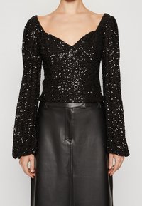 Svart paljett-topp med djup V-ringning, långa puffärmar och texturerat tyg. Matchas med en svart läderkjol med rak skärning.
