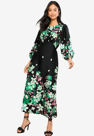 Robe maxi noire à motif floral avec des fleurs vertes, blanches et roses vives. Manches longues bouffantes avec un corsage ajusté et une jupe fluide.