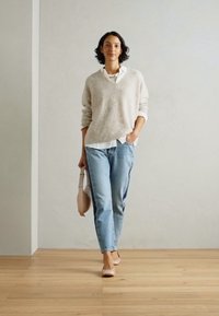 Ανοιχτό γκρίζο πλεκτό πουλόβερ πάνω από ένα λευκό πουκάμισο, συνδυασμένο με ανοιχτό μπλε τζιν. Μια μπεζ τσάντα χειρός και αντίστοιχες μπαλαρίνες ολοκληρώνουν την εμφάνιση.