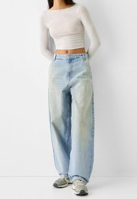 Lehká, dlouhá bílá košile s dlouhým rukávem spárovaná s high-waisted, volnými světlemodrými džínami a šedými teniskami.