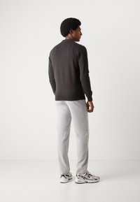 Tamno sivi pulover s visokim ovratnikom, uparen sa svijetlosivim hlačama i bijelim tenisicama. Outfit prikazuje moderan, minimalistički dizajn.