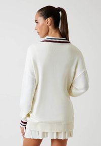 Maglione bianco lavorato a maglia con orlo e polsini a coste, caratterizzato da strisce bordeaux e verdi sul colletto. Design oversize con maniche lunghe.