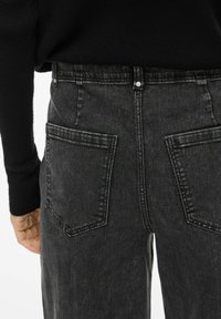 Vaqueros de mezclilla negra con un corte holgado, que cuentan con dos bolsillos traseros y cierre de botón. Tejido texturizado con un acabado desgastado.